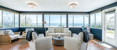 A sunroom with a view of the sea, furnished with a sofa, chairs, and a coffee table.