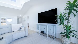 A modern living room with a white sofa, a flat-screen TV on a stand, and a large potted plant. - Ponce Paradise Oceanfront Home (Ponce Inlet)