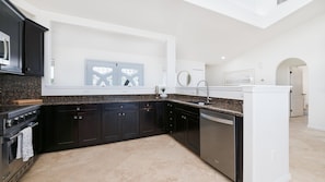 A modern kitchen with dark cabinetry, granite countertops, a built-in oven, and a dishwasher. - Ponce Paradise Oceanfront Home (Ponce Inlet)