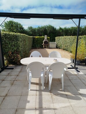 Eine Terrasse im Freien mit einem runden Tisch und weißen Stühlen, umgeben von ordentlich geschnittenen Hecken und einem weißen Zaun.