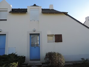 Un edificio con puerta azul, una ventana pequeña con contraventanas y fachada blanca.