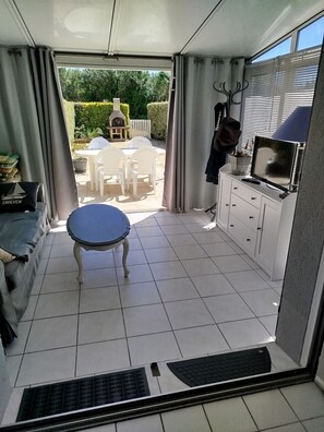Ein Zimmer mit Esstisch und Stühlen, einer Couch, einem Fernseher und Blick ins Freie.