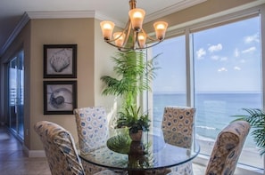 A dining area with a glass table, patterned chairs, a potted plant, and a view of the ocean. - Salida del Sol 1002 in Daytona Beach Shores, FL (Daytona Beach Shores)