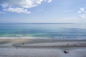 Une plage à l’eau claire, avec un rivage sablonneux et quelques personnes.