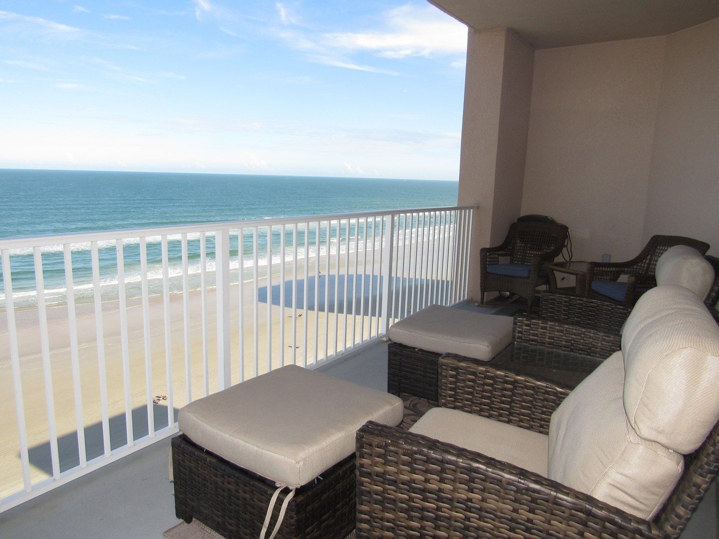 A balcony with wicker furniture, a view of the beach, and a white railing.