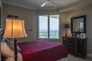 A bedroom with a bed, a dresser, a mirror, and a view of the ocean. - Salida del Sol 1002 in Daytona Beach Shores, FL (Daytona Beach Shores)