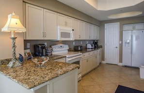 A kitchen with white cabinets, a microwave, a stove, and a refrigerator. - Salida del Sol 1002 in Daytona Beach Shores, FL (Daytona Beach Shores)
