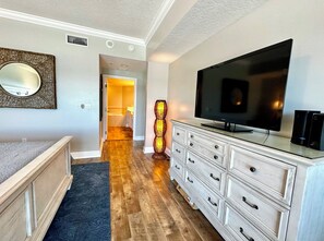 A bedroom with a bed, a dresser, a television, and a decorative floor lamp. - Sanibel Condo #1002 3/3 Direct Oceanfront NE Corner (Daytona Beach Shores)