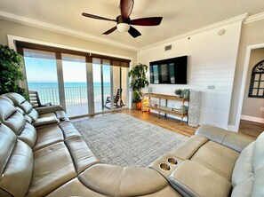 A living room with a large sofa, a television, and a view of the ocean. - Sanibel Condo #1002 3/3 Direct Oceanfront NE Corner (Daytona Beach Shores)