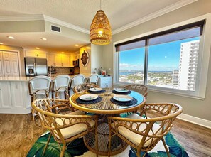 A dining area with a round table, wicker chairs, and a hanging light fixture. - Sanibel Condo #1002 3/3 Direct Oceanfront NE Corner (Daytona Beach Shores)