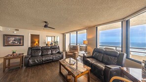 A living room with a leather sofa, a glass coffee table, and a view of the ocean through large windows. - #1004 Seychelles 3/3 Oceanfront Traffic Free Beach (Daytona Beach Shores)