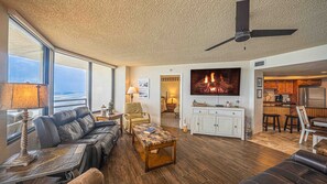 A spacious living area with a leather sofa, a coffee table, and a fireplace. There is a kitchen area with wooden cabinets and a dining table. - #1004 Seychelles 3/3 Oceanfront Traffic Free Beach (Daytona Beach Shores)