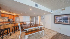 A spacious kitchen with wooden cabinets, a dining area with a wooden table and chairs, and a large framed picture on the wall. - #1004 Seychelles 3/3 Oceanfront Traffic Free Beach (Daytona Beach Shores)