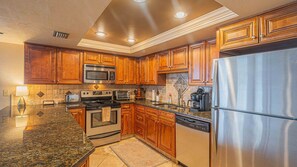 A kitchen with wooden cabinets, stainless steel appliances, granite countertops, and a tiled backsplash. - #1004 Seychelles 3/3 Oceanfront Traffic Free Beach (Daytona Beach Shores)