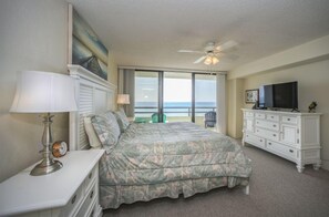 A hotel room with a bed, a TV, a dresser, a lamp, and a view of the ocean through the window. - #1005 Seychelles 2/2 Oceanfront Traffic Free Beach (Daytona Beach Shores)