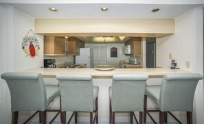 A kitchen with a central island, bar stools, and a welcome sign. - #1005 Seychelles 2/2 Oceanfront Traffic Free Beach (Daytona Beach Shores)
