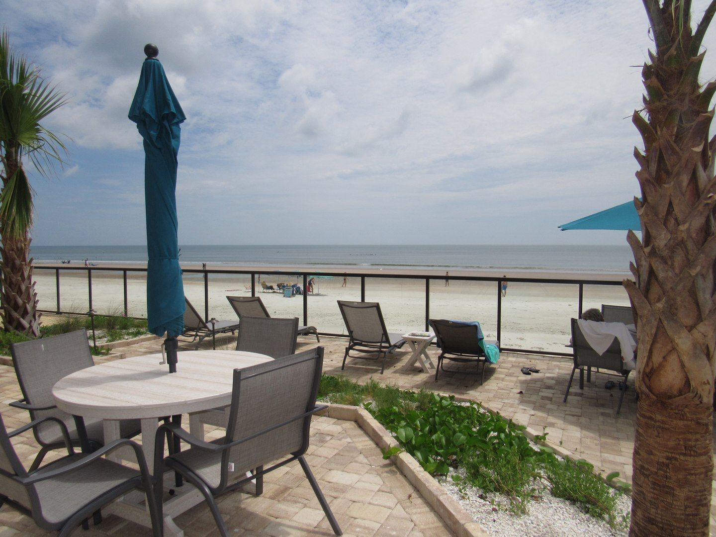 An outdoor seating area with a view of the beach, including a table and chairs, and a statue.