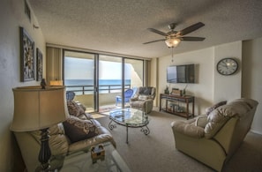 A living room with a sofa, armchair, coffee table, and a ceiling fan. - #1005 Seychelles 2/2 Oceanfront Traffic Free Beach (Daytona Beach Shores)