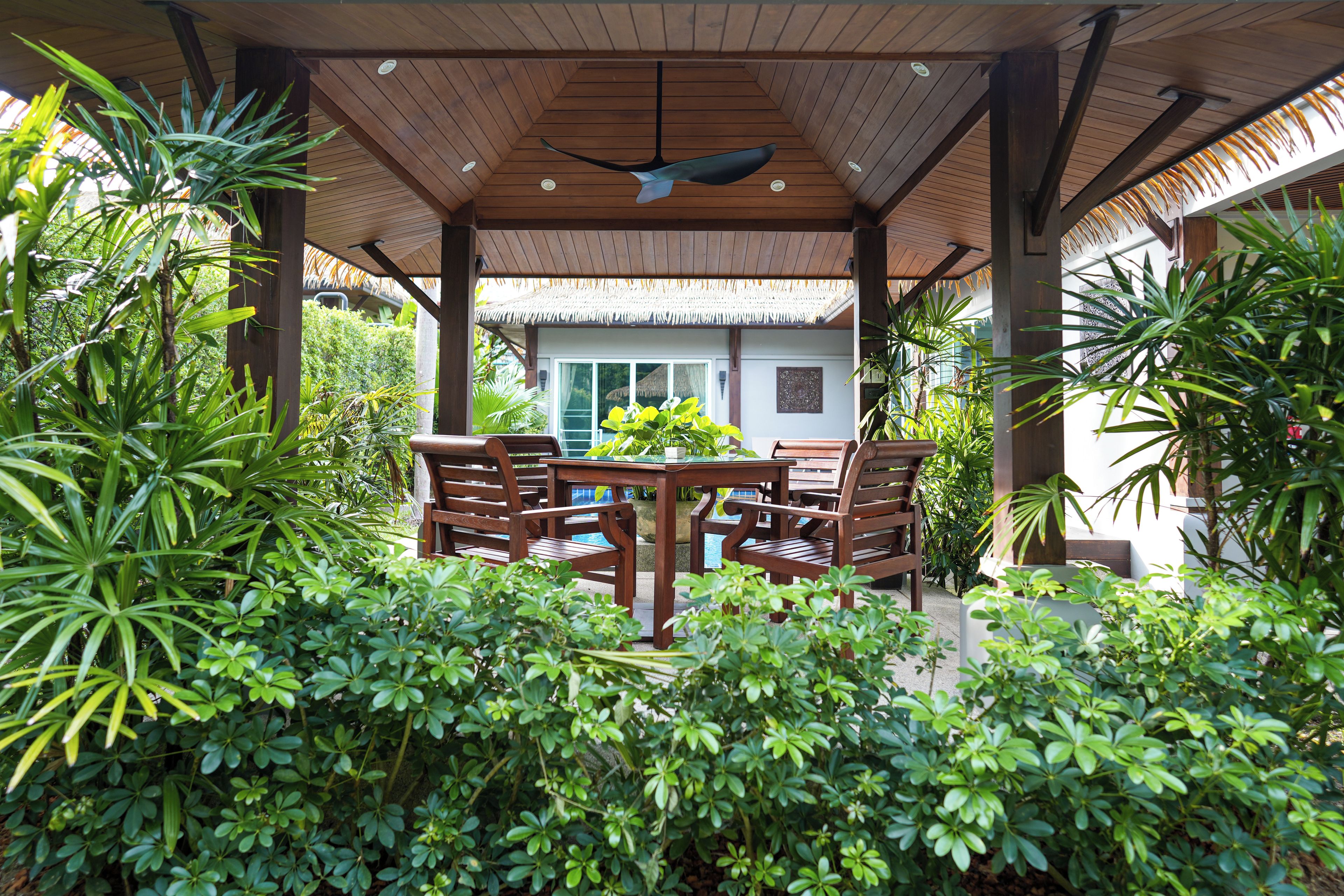 Un espace extérieur aménagé, abrité et doté de mobilier en bois et d’une végétation luxuriante.