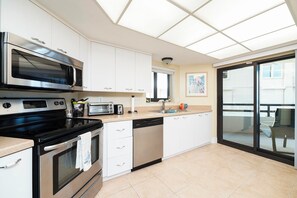A modern kitchen with a built-in oven, microwave, and toaster. It features white cabinetry, a large window, and a sliding glass door leading to an outdoor area. - #101 Seychelles 2/2 Oceanfront Traffic Free Beach (Daytona Beach Shores)