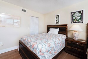 Un dormitorio con una cama, una mesita de noche, una lámpara y dos cuadros en la pared.