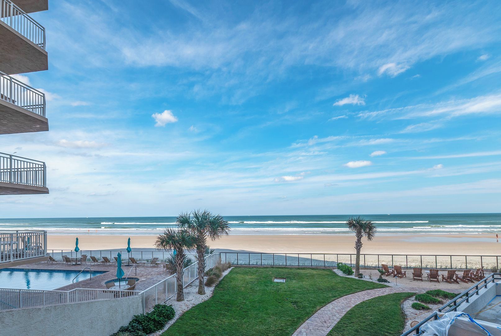 A beachfront property with a swimming pool, lounge chairs, and a view of the ocean.