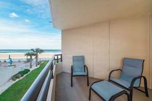 A balcony with two chairs, a view of the beach, and a palm tree. - #101 Seychelles 2/2 Oceanfront Traffic Free Beach (Daytona Beach Shores)