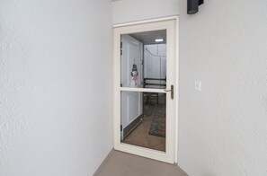Une porte blanche avec un panneau de verre, donnant sur une pièce où l’on aperçoit une chaise et un tapis à motifs.