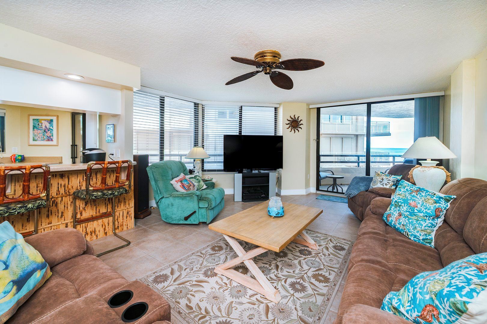 A living room with a sofa, a television, a ceiling fan, and a bar area with stools.