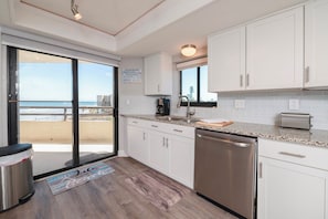 Eine moderne Küche mit Blick auf den Strand, weißen Schränken, Edelstahlgeräten und einem großen Fenster.