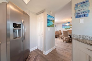 Eine moderne Küche mit einem Edelstahl-Kühlschrank, ein Essbereich mit Korbstühlen und eine Wand mit dem Schriftzug 'Life's at ease with an ocean breeze'.