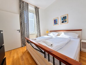 A bedroom with a wooden bed frame, white bedding, a window with polka dot curtains, and two framed pictures on the wall. - Your Vienna Home 2BR near Stadthalle (Vienna)