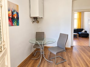 A room with a glass-top table and two chairs, a painting on the wall, and a sofa in the background. - Your Vienna Home 2BR near Stadthalle (Vienna)