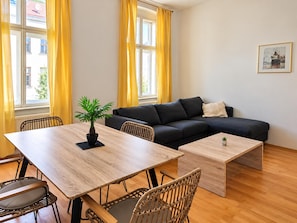 A modern living room with a wooden dining table, a sofa, and a small potted plant. - Your Vienna Home 2BR near Stadthalle (Vienna)