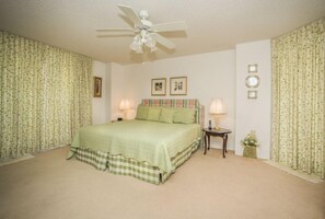 Ein Schlafzimmer mit einem Bett, zwei Nachttischen, einem Deckenventilator und Vorhängen mit Blumenmuster.