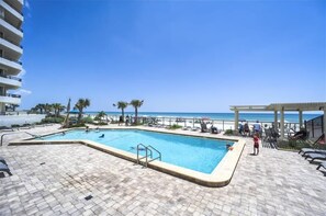 Ein Swimmingpool mit Blick auf den Strand, umgeben von Liegestühlen und Palmen.