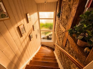 Una escalera de madera con vistas a la vegetación exterior, un muro de piedra y una ventana.