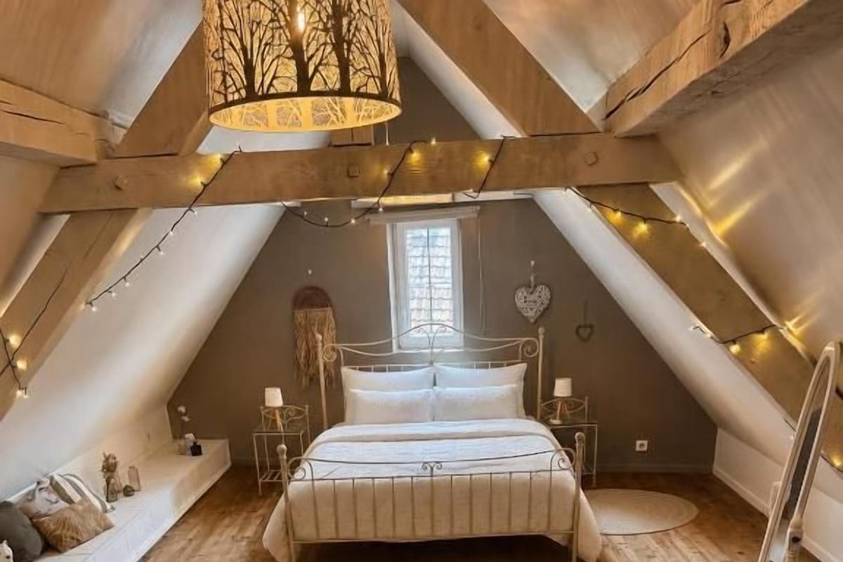 A bedroom with a sloped ceiling, a bed, a bedside table, a lamp, and a window.