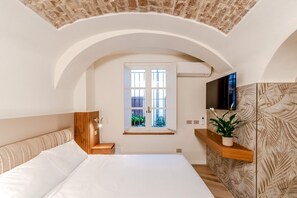 Een slaapkamer met een groot bed, een houten hoofdbord, een raam, een flatscreen televisie en een plant op een plank.