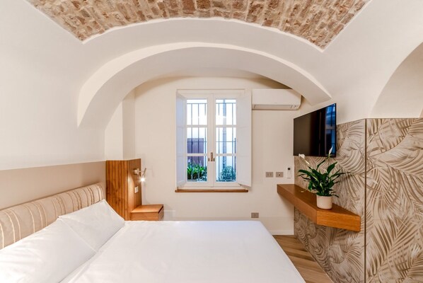 A bedroom with a large bed, a wooden headboard, a window, a flat-screen TV, and a plant on a shelf.