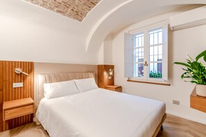 A bedroom with a bed, bedside tables, a window with a view, and a plant.