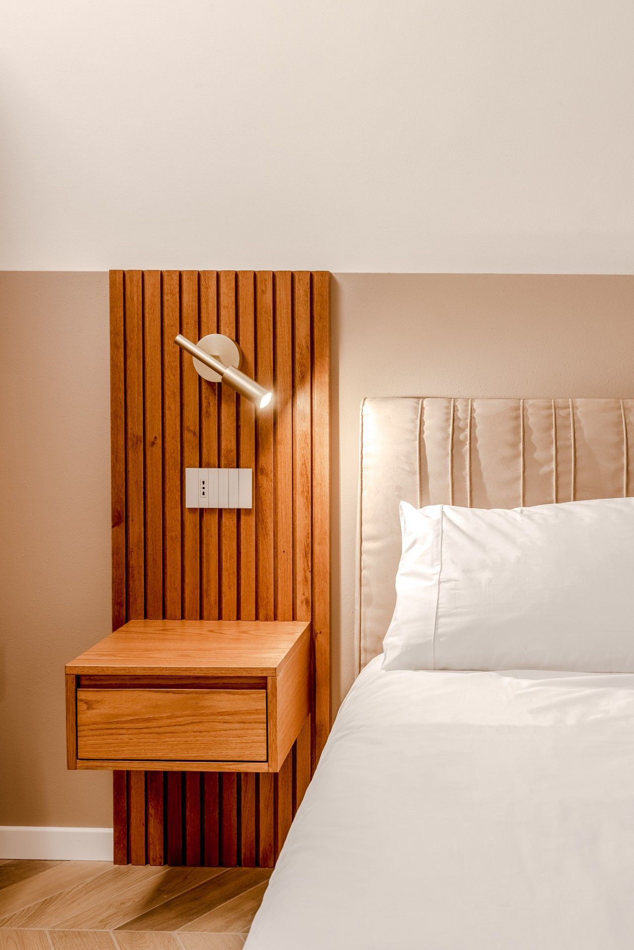 Una camera da letto con un comodino in legno, una lampada a parete e un letto con biancheria da letto bianca.