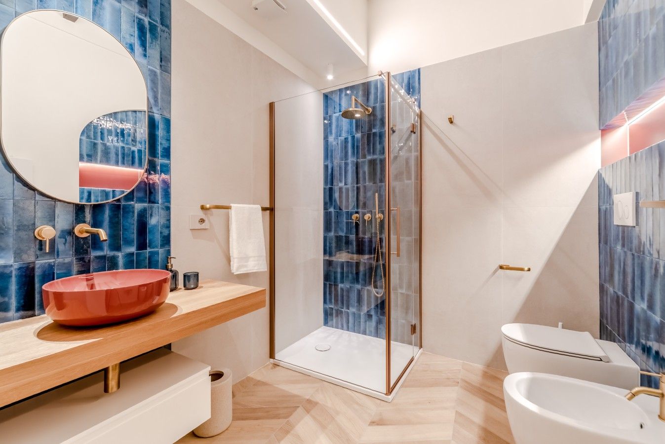 Een moderne badkamer met een douchecabine van glas, een houten wastafelmeubel met een rode wasbak en een wit toilet.