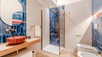 Een moderne badkamer met een douchecabine van glas, een houten wastafelmeubel met een rode wasbak en een wit toilet.