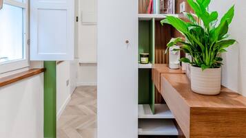 Ein Flur mit Holzboden, einer weißen Tür und einer grünen Regalwand mit Büchern und einer Pflanze.