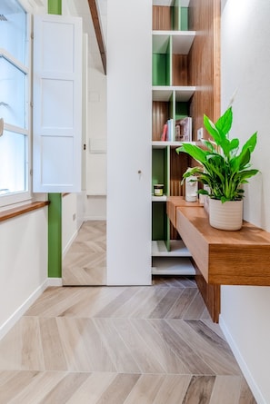 A hallway with a wooden floor, a white door, and a green shelf unit with books and a plant. - Parco Ducale Design Rooms - Queen Room (Parma)