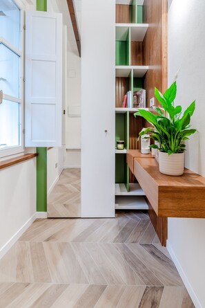 A hallway with a wooden floor, a white door, and a green shelf unit with books and a plant. - Parco Ducale Design Rooms - King Room (Parma)