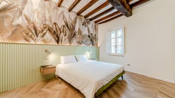 A bedroom with a bed, a nightstand, a wall with a leaf pattern, a window, and wooden beams on the ceiling.