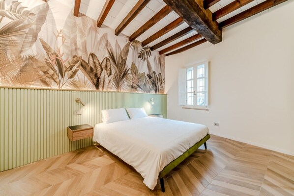Een slaapkamer met een bed, een nachtkastje, een muur met een bladmotief, een raam en houten balken in het plafond.