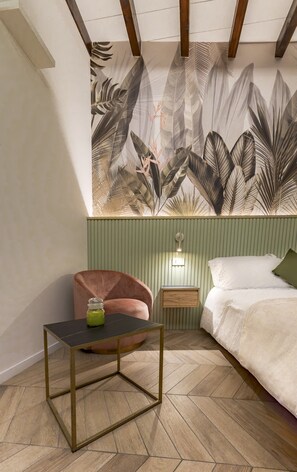 Een slaapkamer met een bed, een stoel, een klein tafeltje en een wand met een bladmotief.